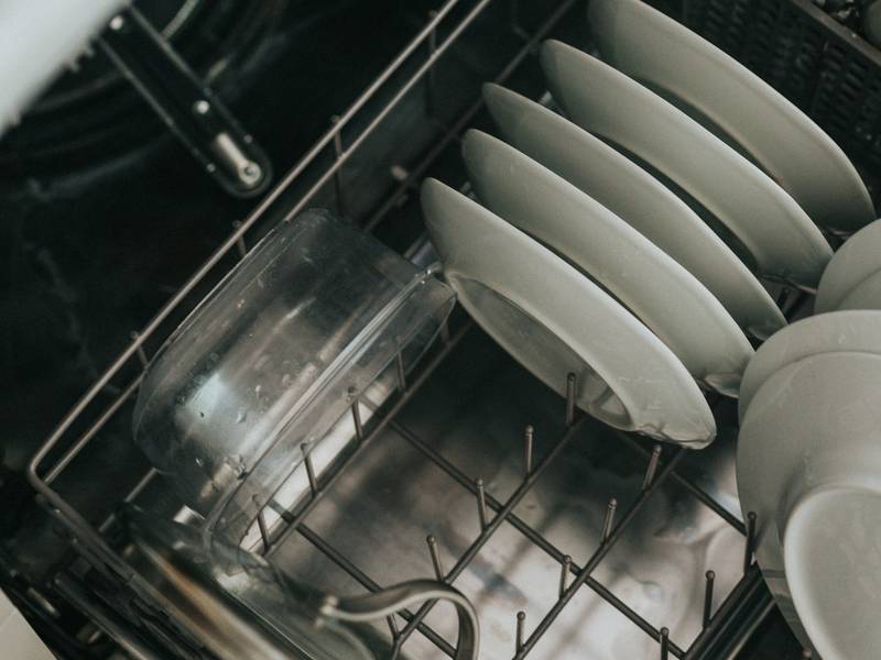 Clean white plates and a glass in an open dishwasher rack.
