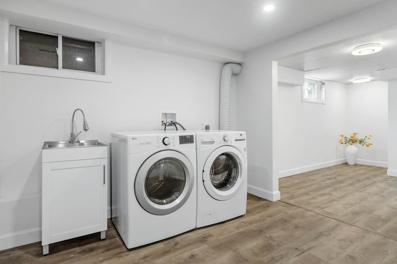 A bright, clean laundry room with a white front-load washer and dryer beside a utility sink.