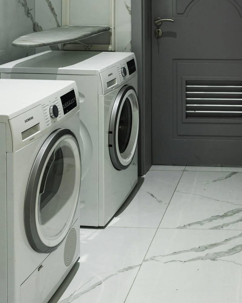 Two white front-load laundry machines side by side on a marble-look floor.